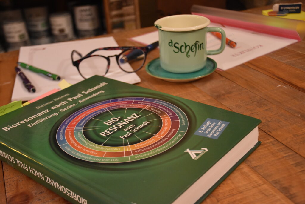 Tisch auf dem verschiedene Requisiten wie eine Brille, Papier, eine Tasse und ein Buch &uuml;ber Bioresonanz liegt