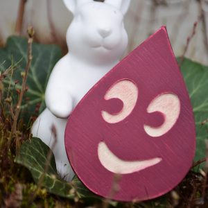 Weißer Osterhase hält roten Tropfen mit lachendem Gesicht