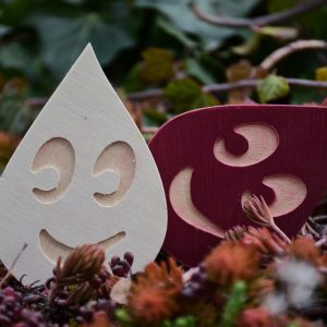 Zwei Tropfen-Anhänger, einer lächelnd, einer rot, im Grünen