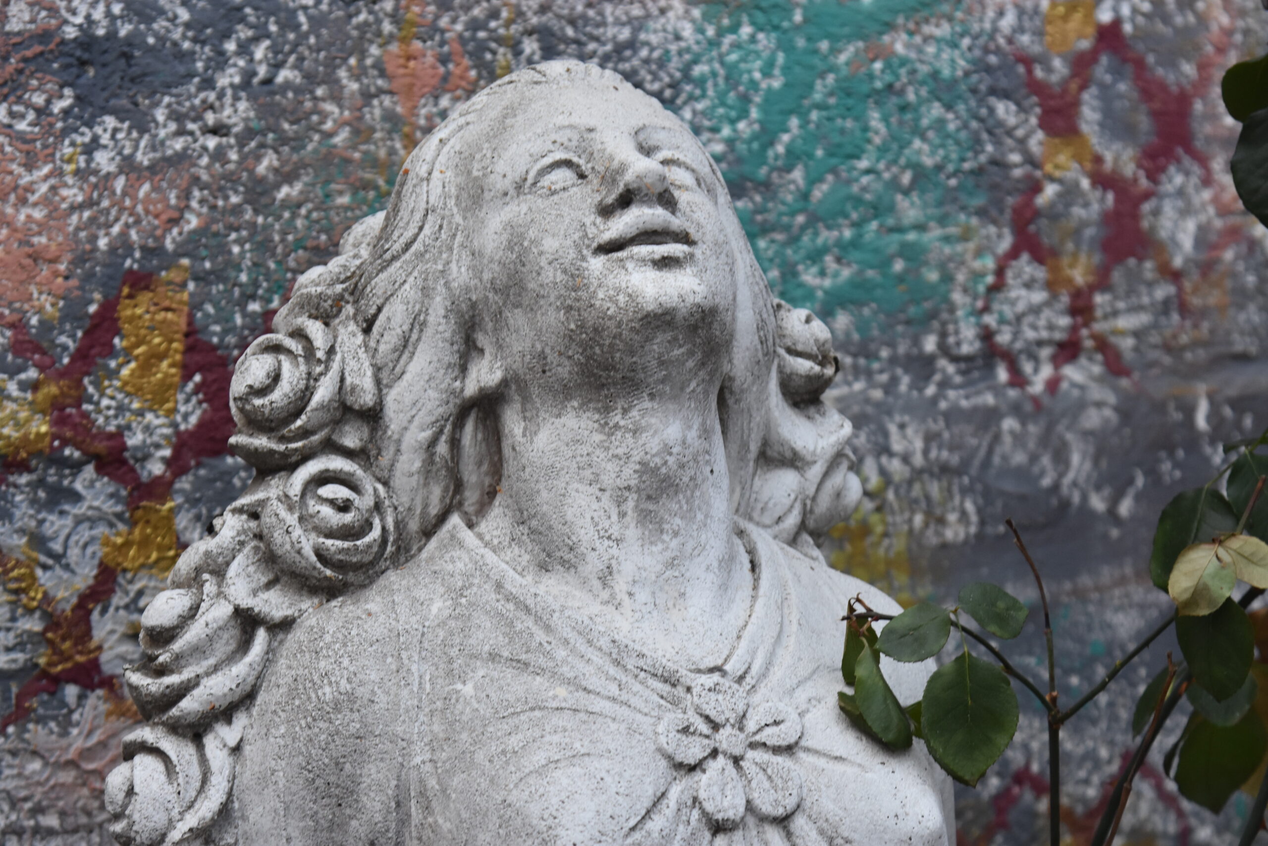 DSC_0730 Steinstatue einer Frau mit Rosen im Haar vor einer bunten Wand